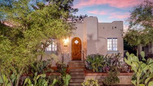 Un bâtiment recouvert d’enduit, avec une porte en bois, entouré de différents types de cactus et de plantes du désert.