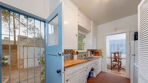Une cuisine de taille réduite avec des meubles blancs, un plan de travail en bois et une porte bleue donnant sur un espace extérieur clos.