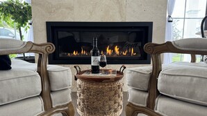 Una sala de estar acogedora con chimenea, dos sillones tapizados, una mesa de centro de fibras naturales y una botella de vino.