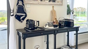 Comedor con una mesa negra dispuesta con diversos utensilios de cocina, un cuadro en la pared y vista a una piscina exterior.