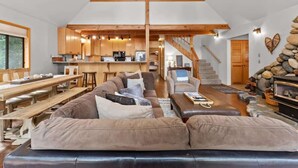 A spacious living area with a large sofa, a dining table, and a kitchen in the background. - Tranquil Tahoe A-Frame, Walk to Beach! (Tahoe Vista)