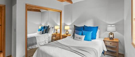 A bedroom with a large bed, two bedside tables with lamps, a mirror, and a door.