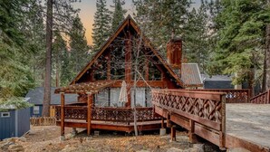 A rustic cabin with a wooden deck, surrounded by tall pine trees. - Tranquil Tahoe A-Frame, Walk to Beach! (Tahoe Vista)