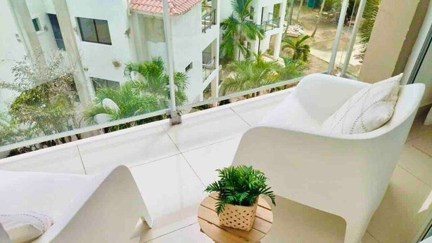 A balcony with two white chairs and a small wooden table with a plant.
