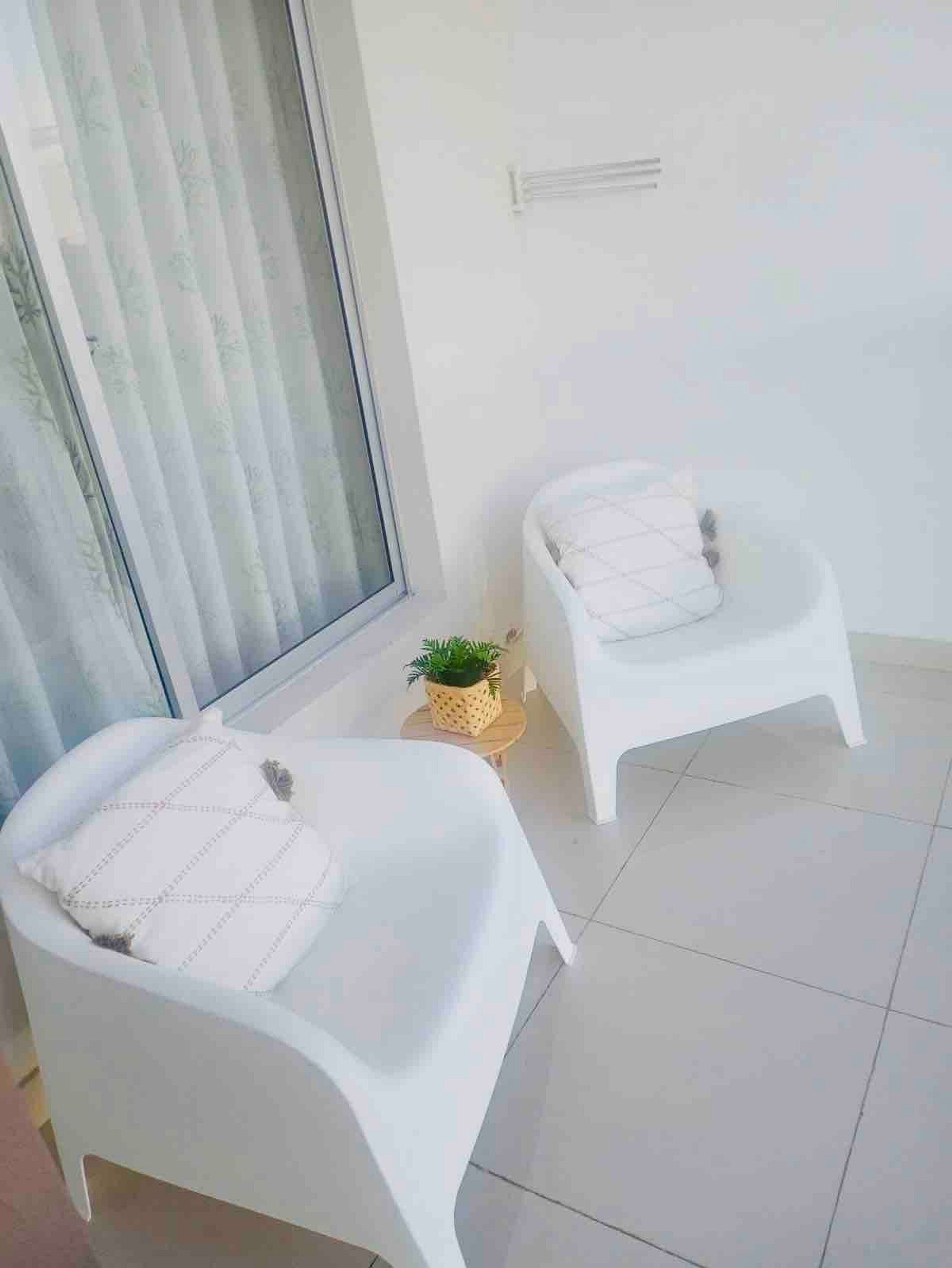 A balcony with two white chairs and a small potted plant.