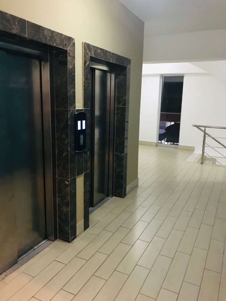 A hallway with two elevators, a handrail, and a tiled floor.