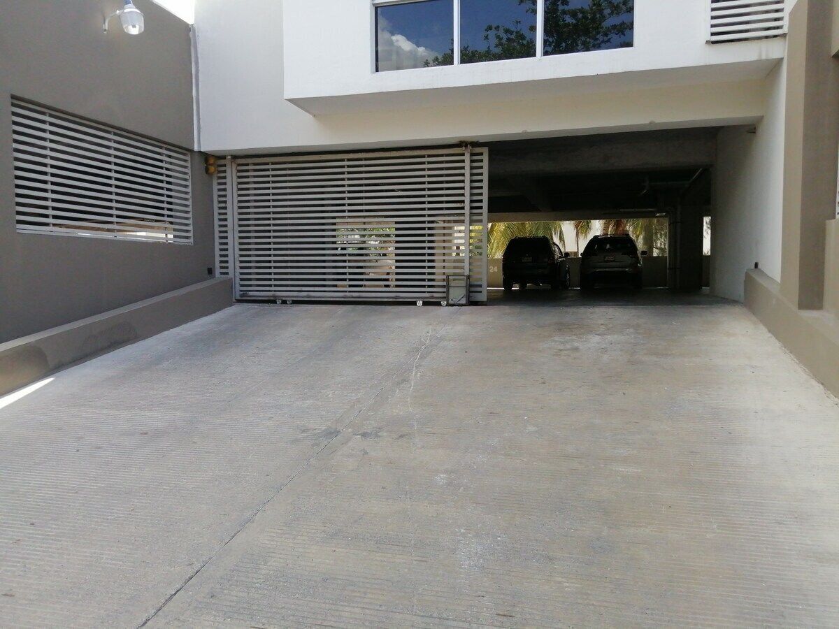 A covered parking area with a concrete floor, a metal gate, and a car parked inside.