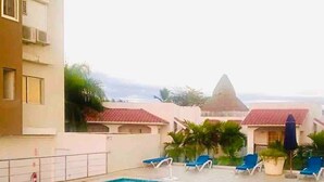 A swimming pool with blue water, surrounded by lounge chairs and a building with a red-tiled roof.