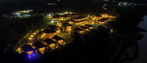 An aerial view of a resort with multiple buildings, a swimming pool, and a well-lit beachfront area.
