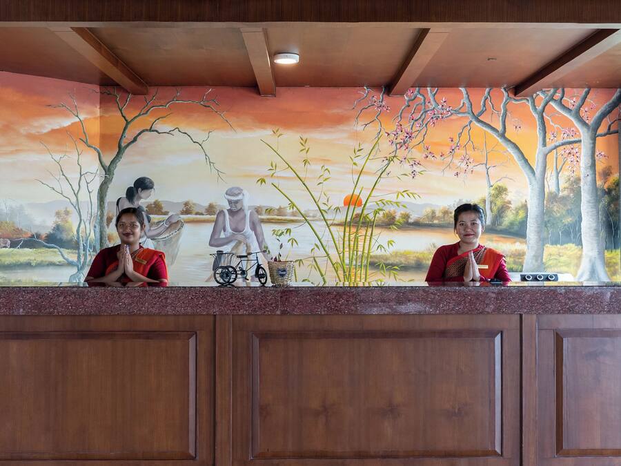 Bancada de recepção com um mural que retrata uma paisagem com água, árvores e pôr do sol.
