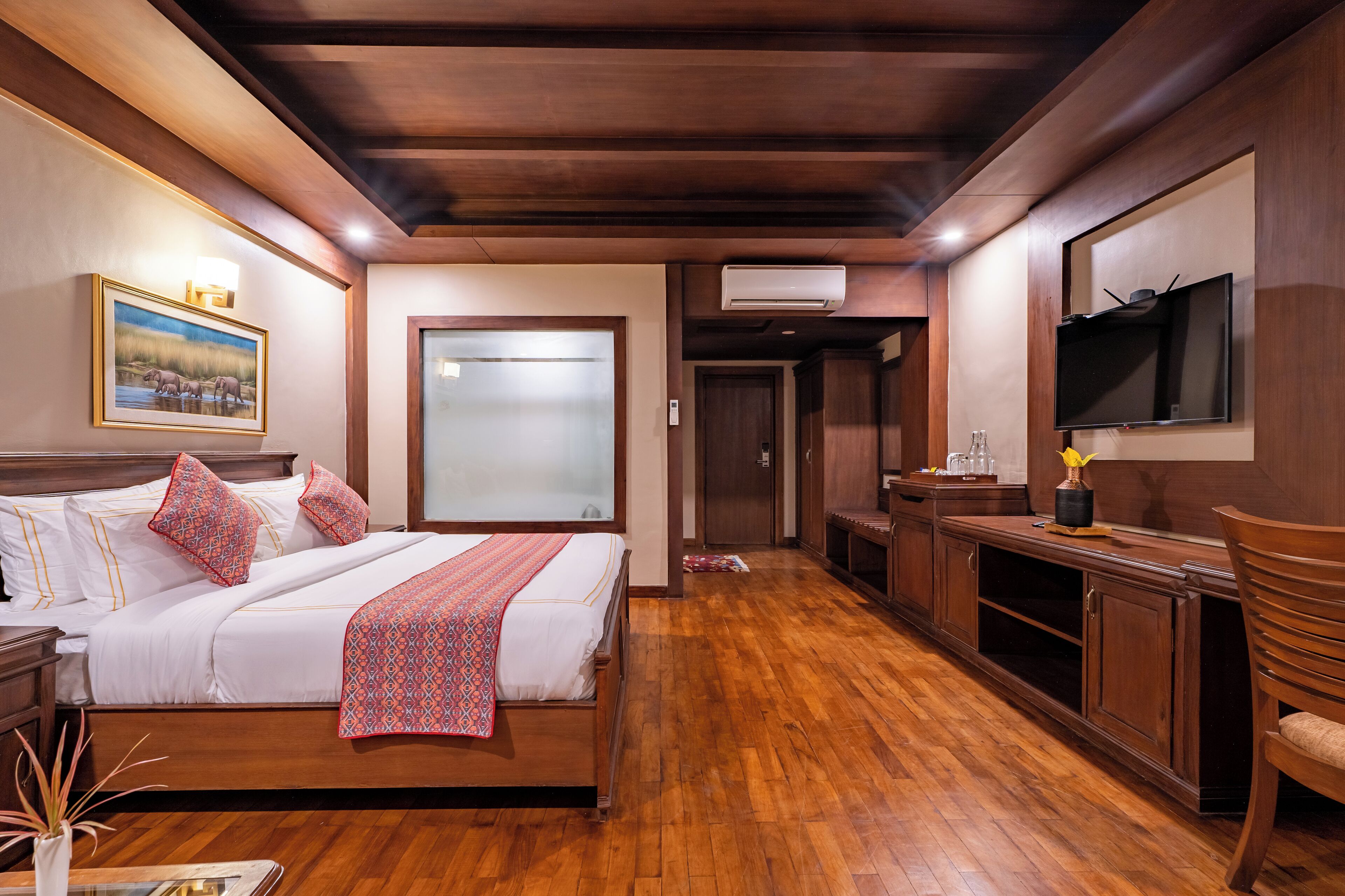 A hotel room with a wooden bed, a TV mounted on the wall, and a wooden desk.