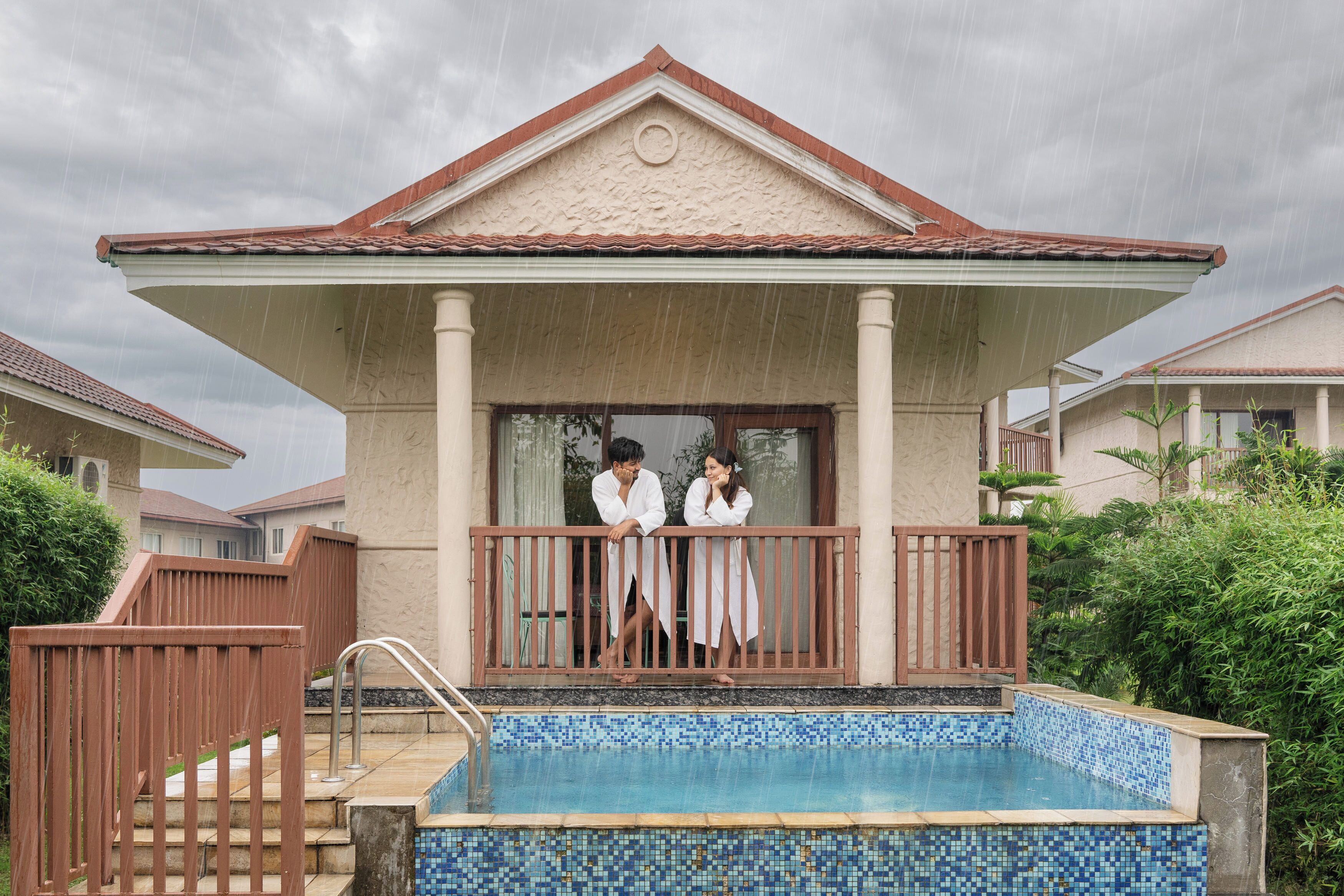 A pool area with a tiled deck, a covered seating area, and a building with a tiled roof.