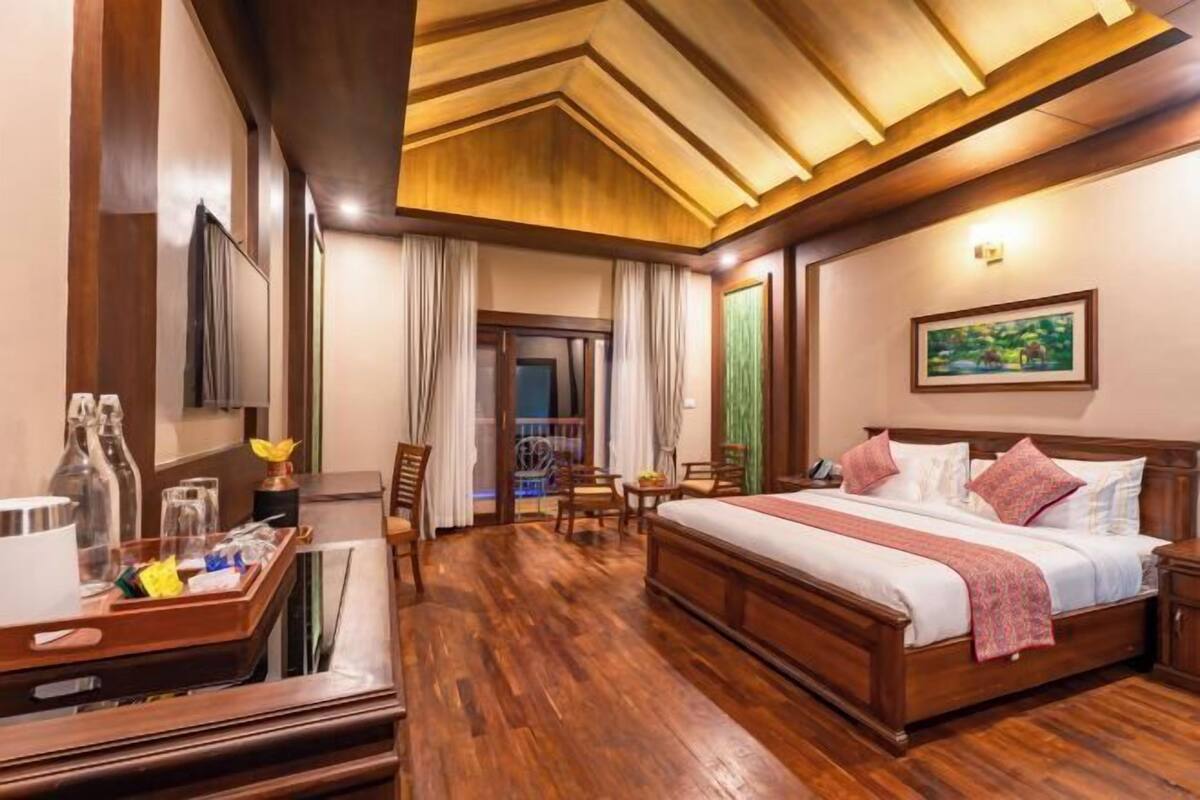 Une chambre d’hôtel avec un lit en bois, un bureau sur lequel se trouve un plateau avec divers objets, une chaise et une vue sur l’extérieur.