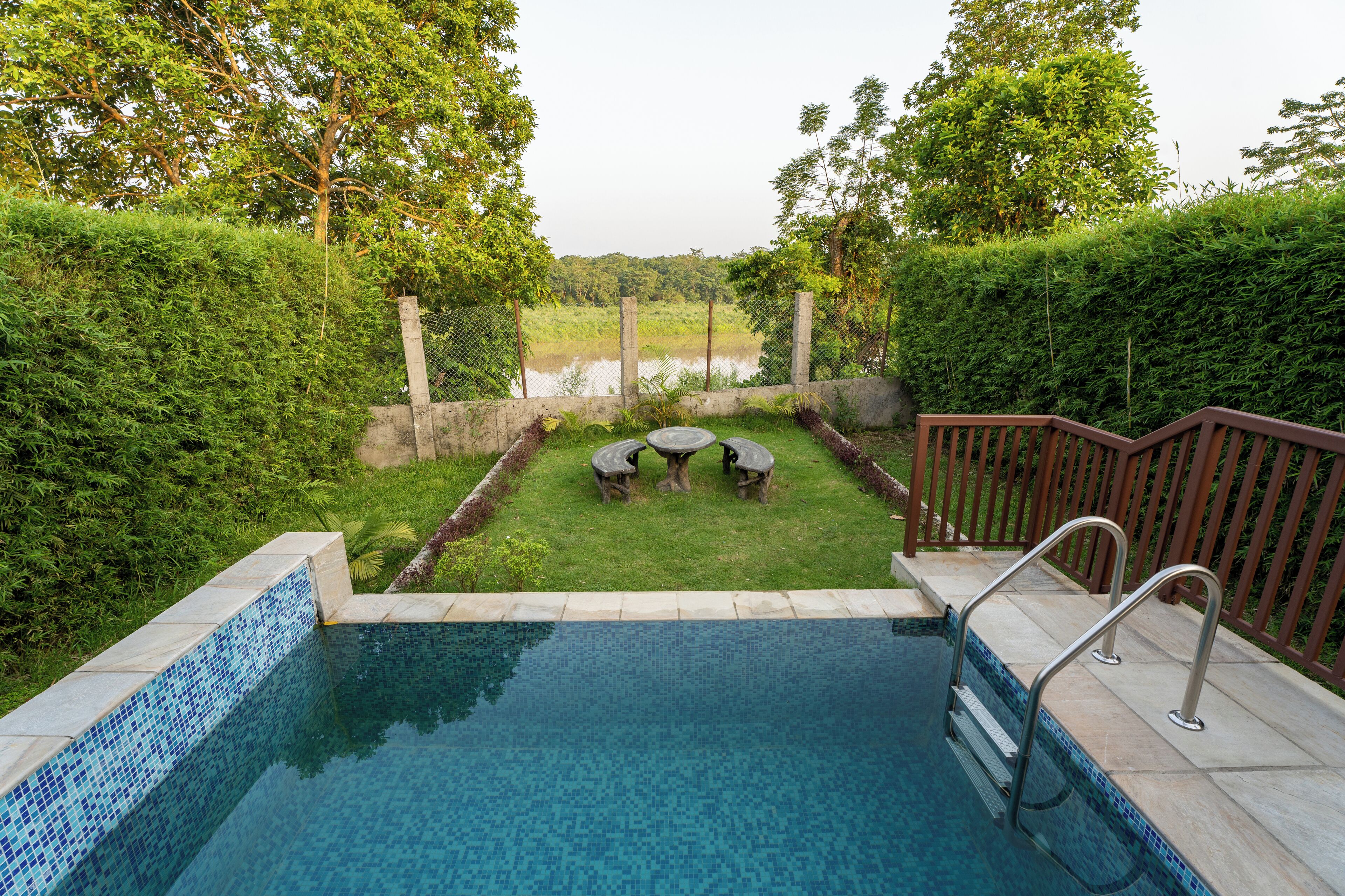 Una piscina con borde de azulejos, rodeada de césped y una terraza de madera.