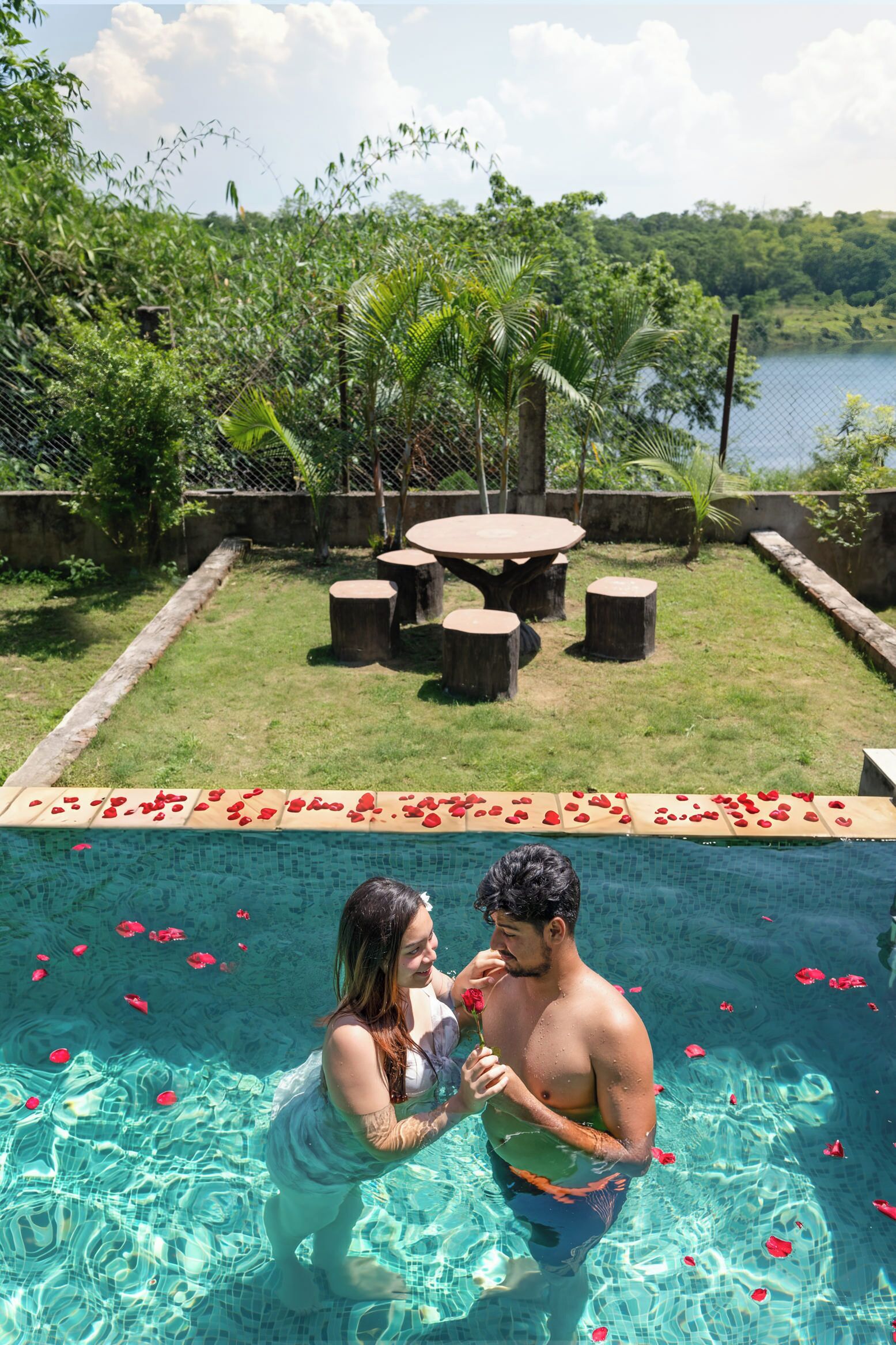 A swimming pool with clear water, surrounded by greenery and a view of a lake.