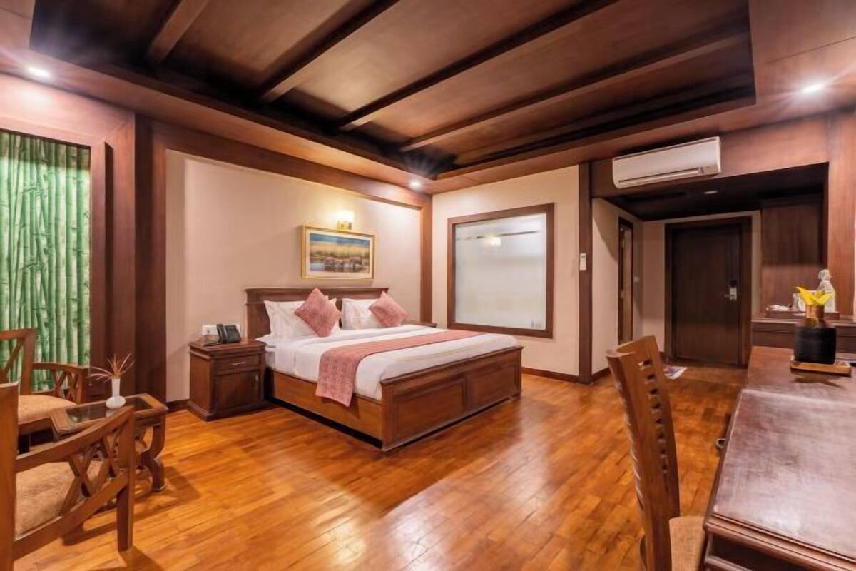 Une chambre à coucher avec un lit en bois, des tables de chevet, une chaise, une table à manger et une grande fenêtre.
