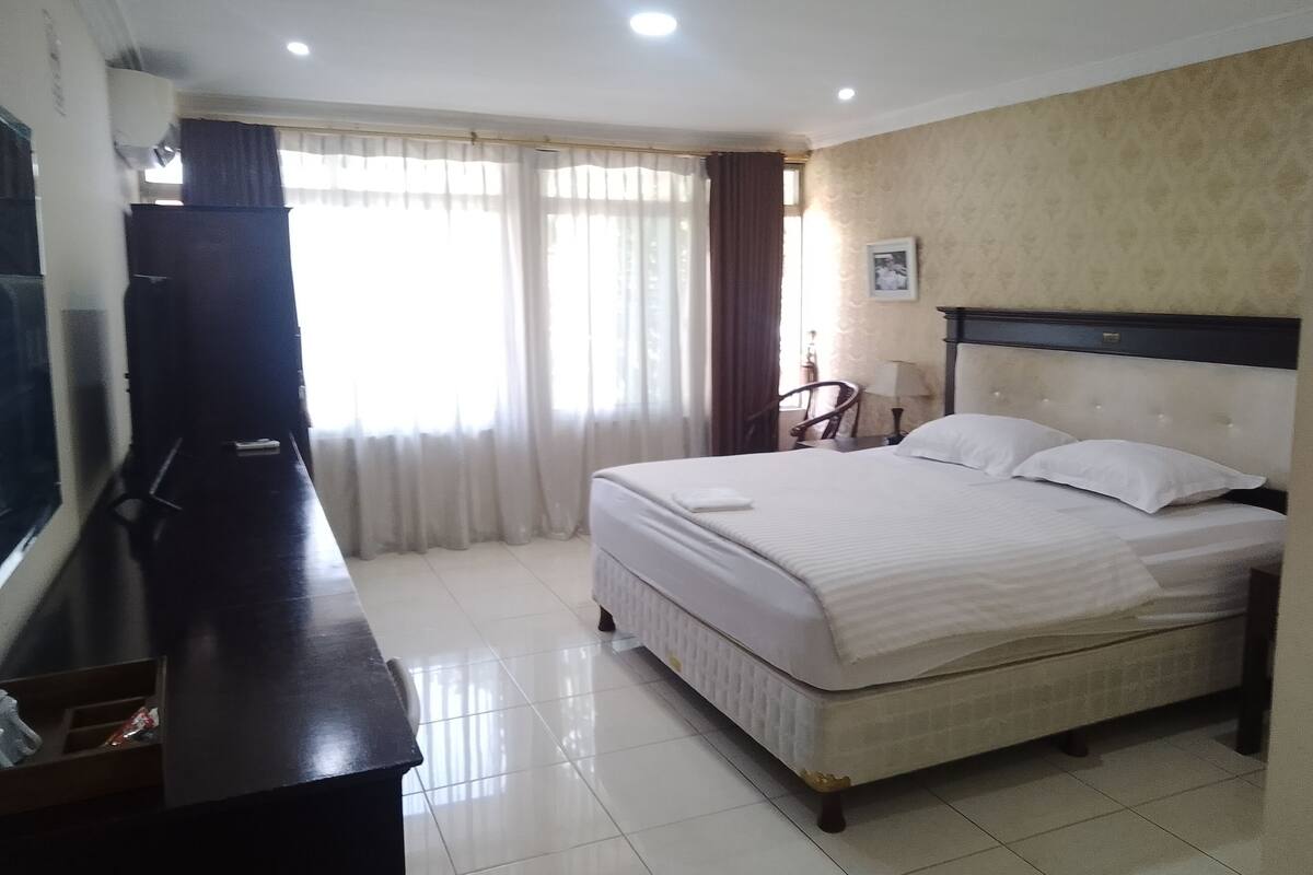 A hotel room with a bed, a desk, a chair, a TV, and a window with curtains.