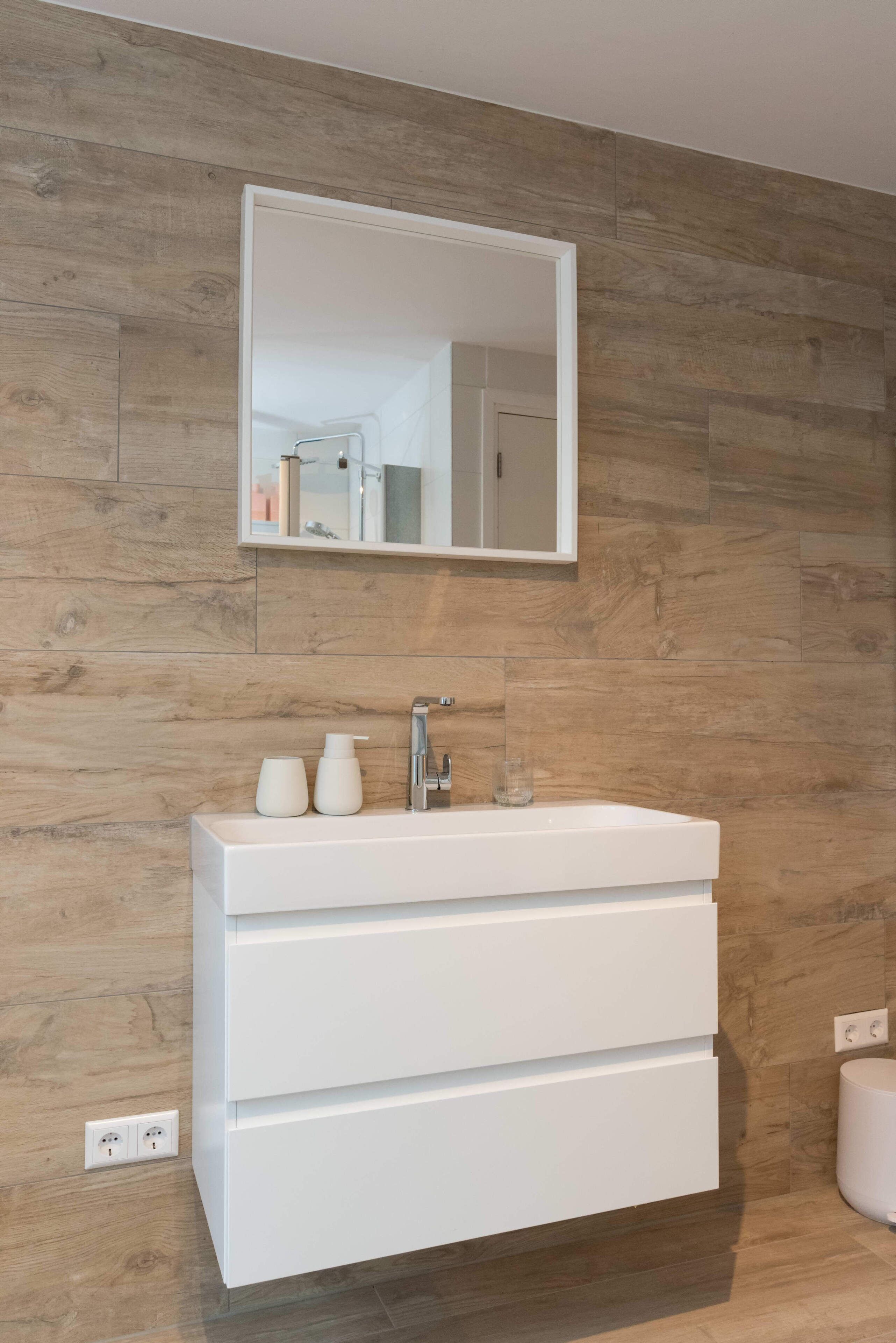 A bathroom with a white vanity, a mirror, and a wooden wall.