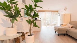 A modern living room with a sofa, a coffee table, and two potted plants. There is a dining area with a chair and a table in the background. - Studio Loet Schagen (Schagen)