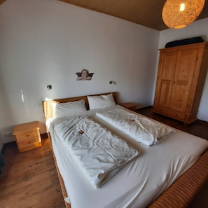 A bedroom with a wooden bed, a nightstand, a wardrobe, and a wall-mounted light fixture.