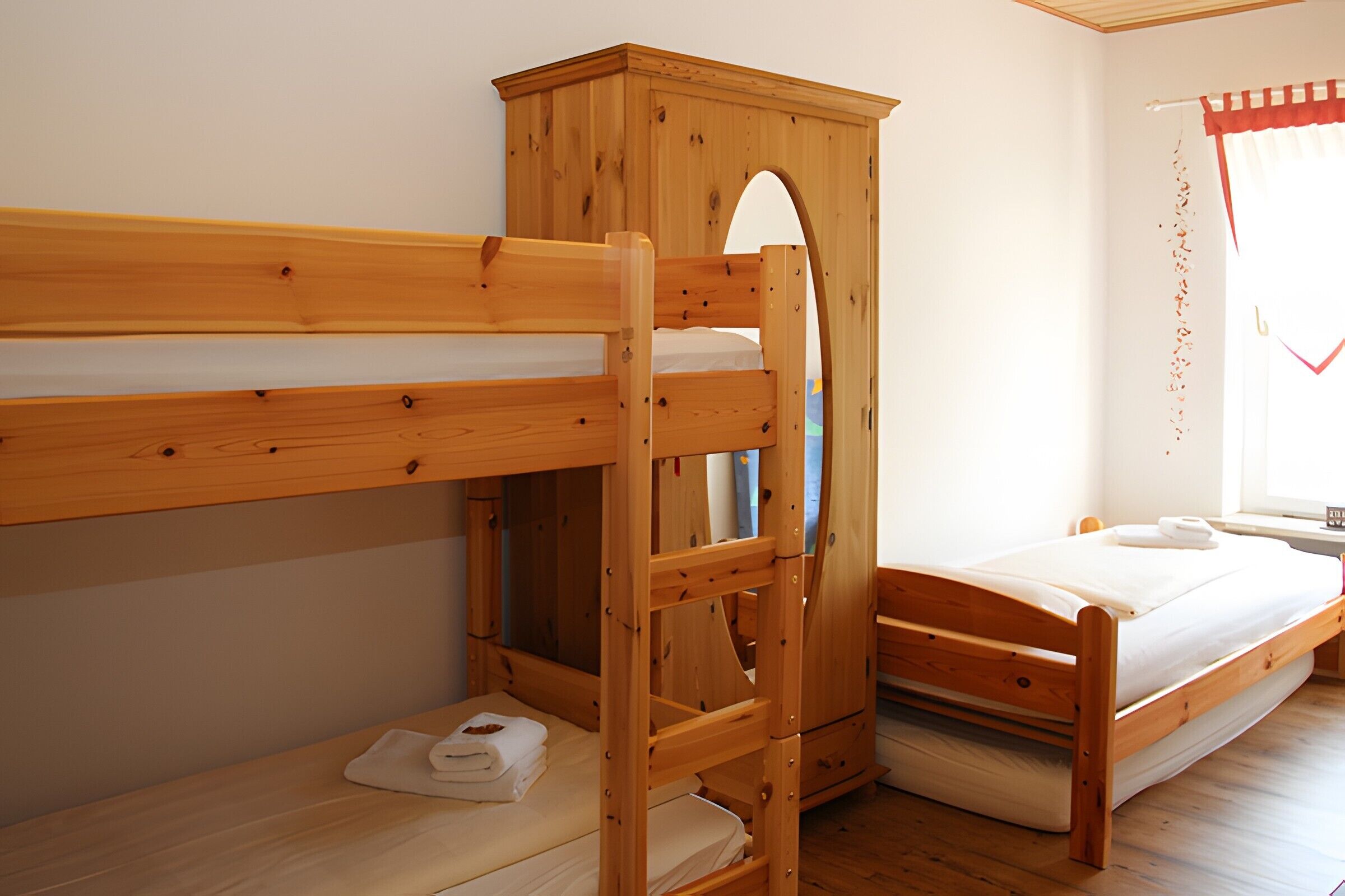 Una cama individual con literas, un armario de madera y una ventana con cortinas.