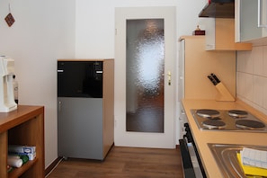 A compact kitchen with a refrigerator, stove, and wooden shelving.