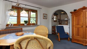 Un coin repas avec des chaises en osier, une table en bois et une vue sur la campagne, grâce à de grandes fenêtres.