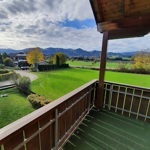 A balcony with a view of a green field, a building, and mountains in the distance.