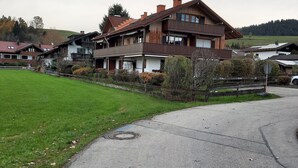 Une maison en bois à deux étages, dotée d’un balcon, entourée d’une pelouse et bordée d’un chemin pavé.