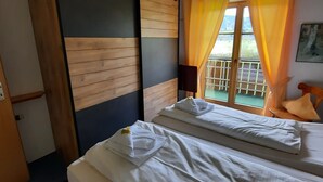 Une chambre d’hôtel avec un lit, une armoire en bois, une fenêtre avec des rideaux et un balcon doté d’une balustrade.