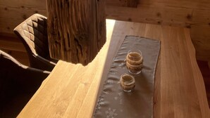 L’intérieur d’un chalet en bois, avec une table à manger, des chaises et une vue sur des montagnes enneigées, visible par une fenêtre.