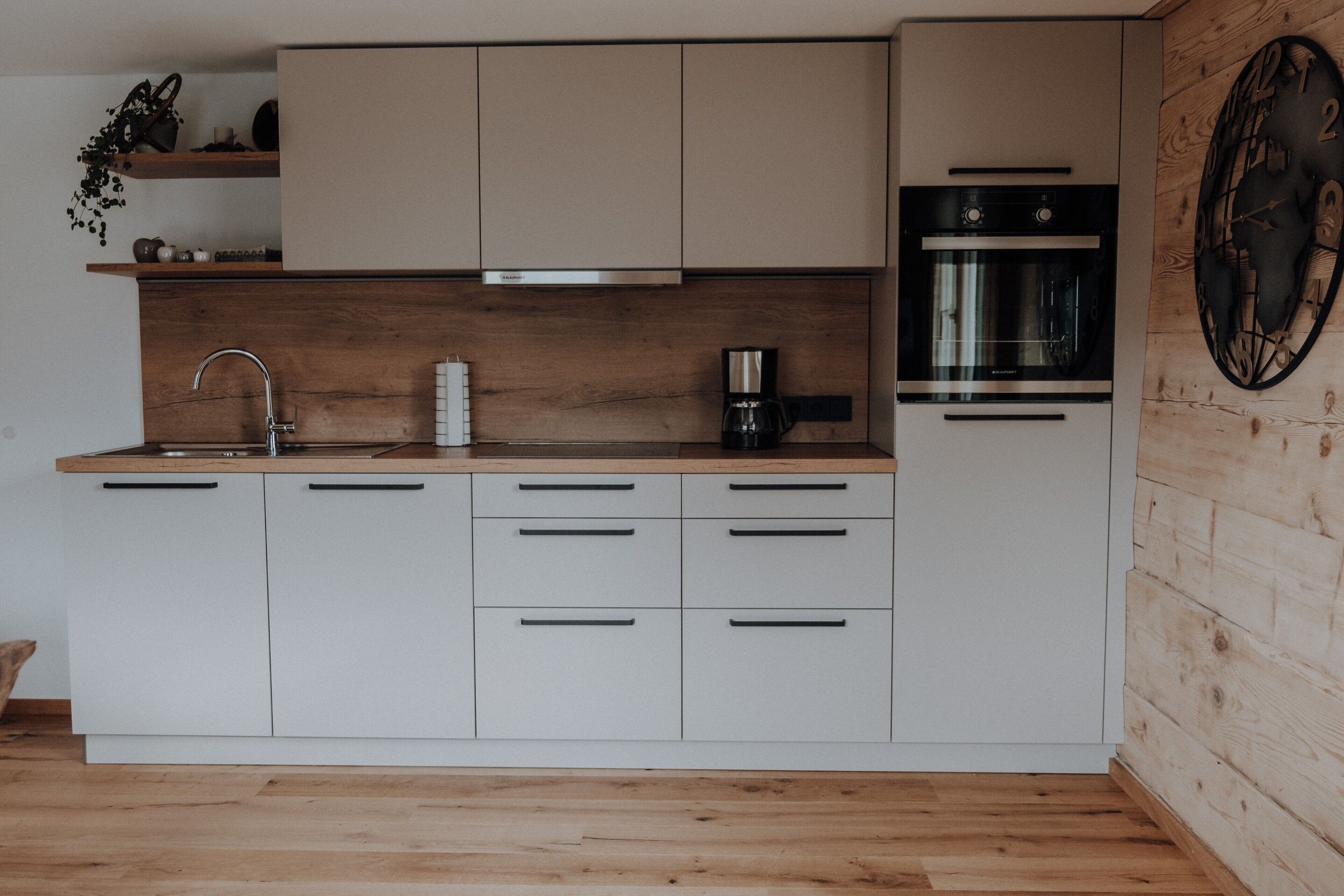 A modern kitchen with wooden cabinets, a stainless steel sink, a coffee maker, and a clock on the wall.