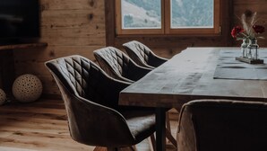Une table à manger en bois, quatre chaises, un vase avec des fleurs et une fenêtre donnant sur une vue sur les montagnes.