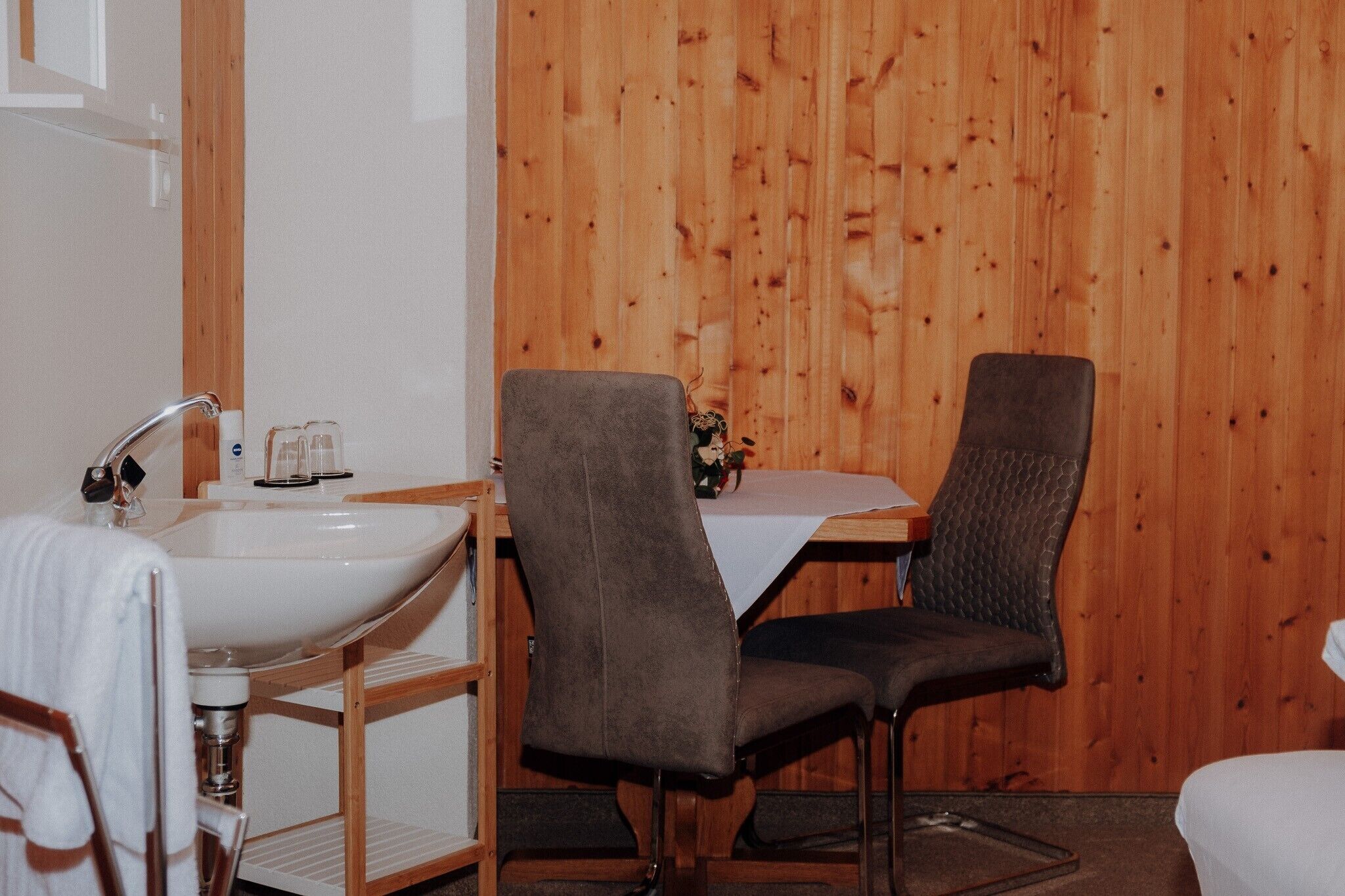 Ein Badezimmer mit Waschbecken, zwei Stühlen und einer Holzwand.