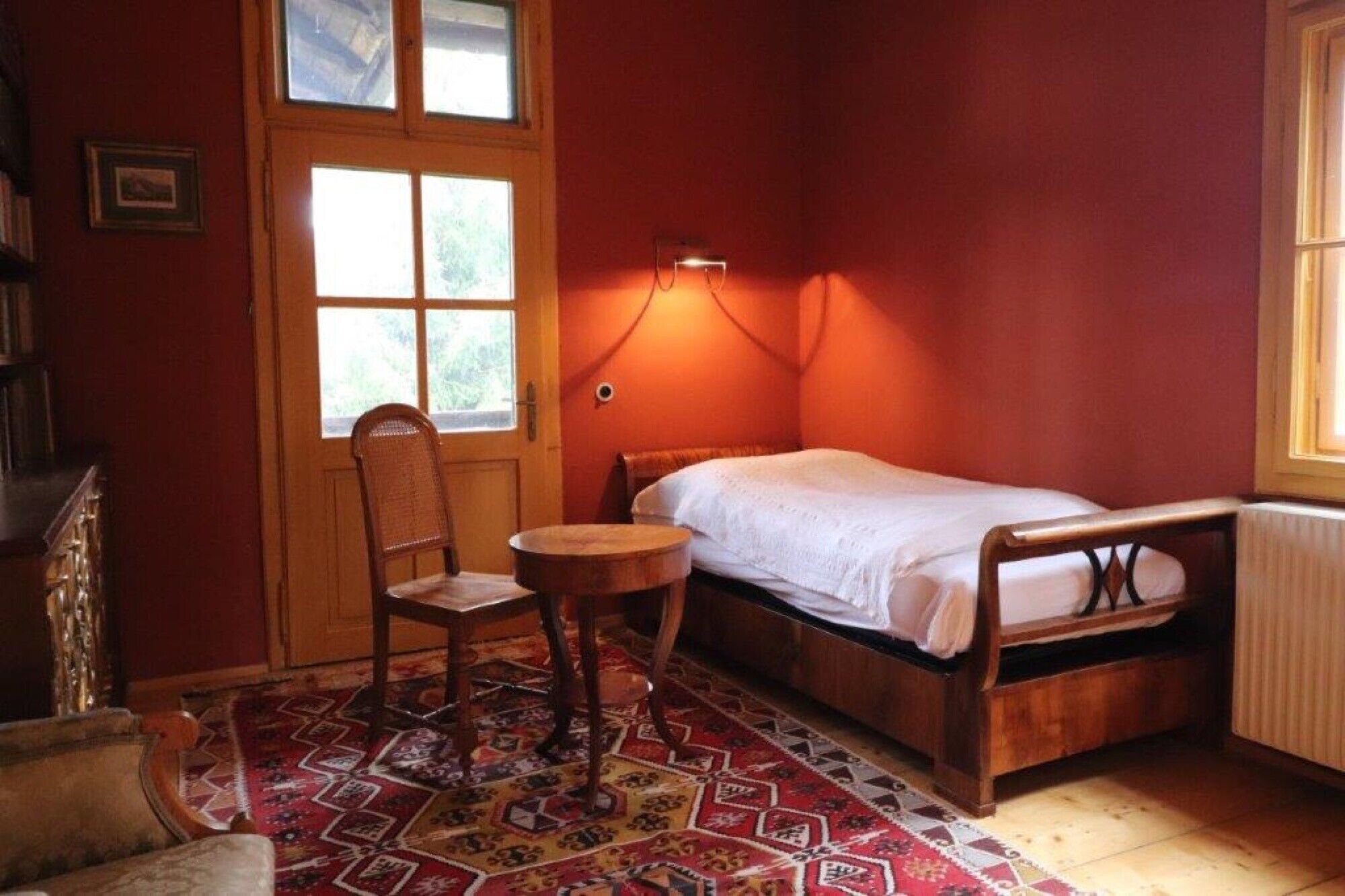 Een kleine kamer met een eenpersoonsbed, een stoel, een tafel en een raam.