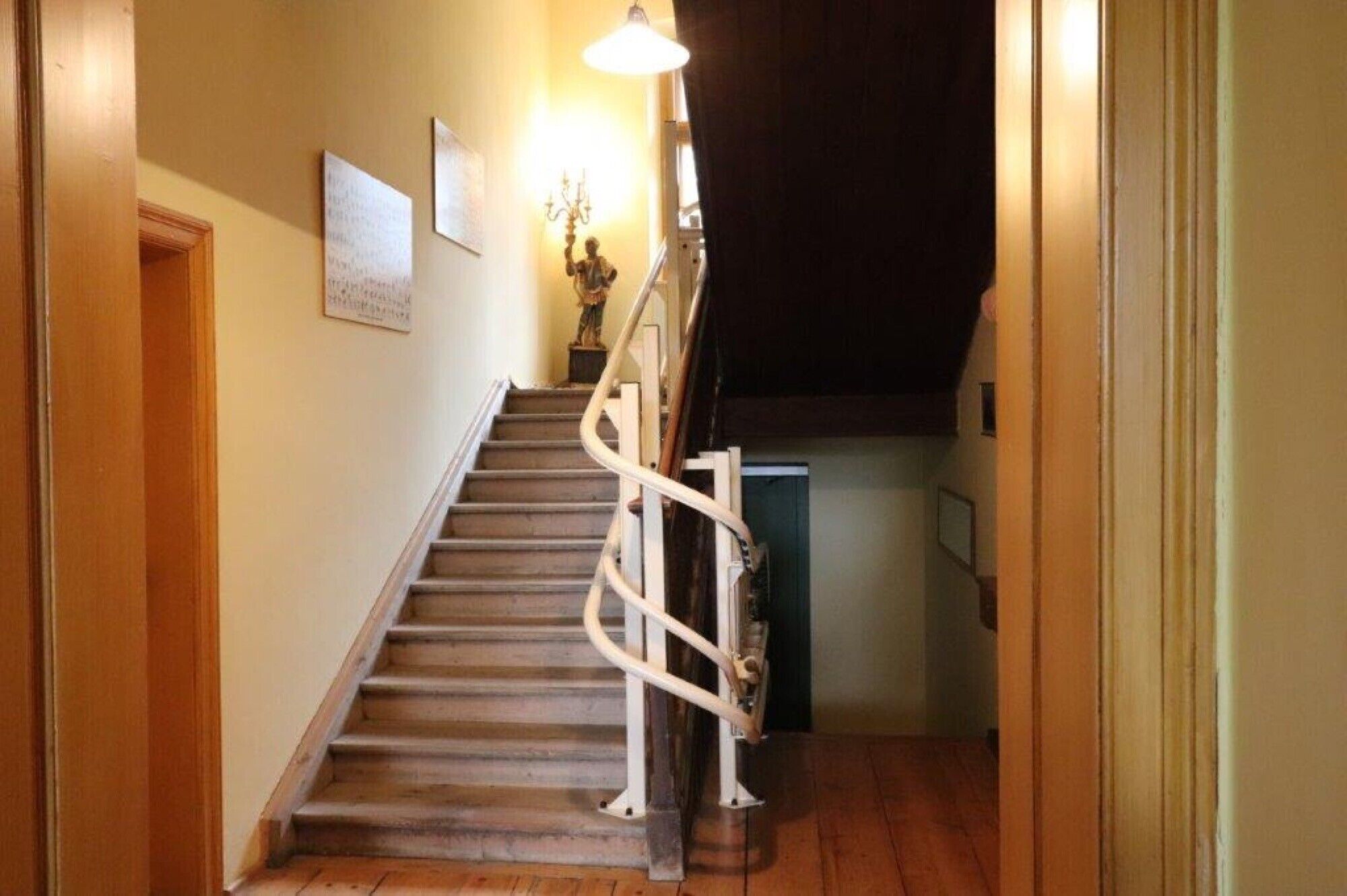 A wooden staircase with a handrail, a wall-mounted light fixture, and a door at the bottom.