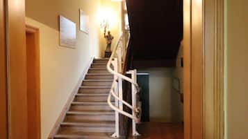 A wooden staircase with a handrail, a wall-mounted light fixture, and a door at the bottom.