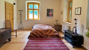 Une chambre à coucher avec un lit, un radiateur, un plancher en bois, une fenêtre, un porte-manteau et une porte.