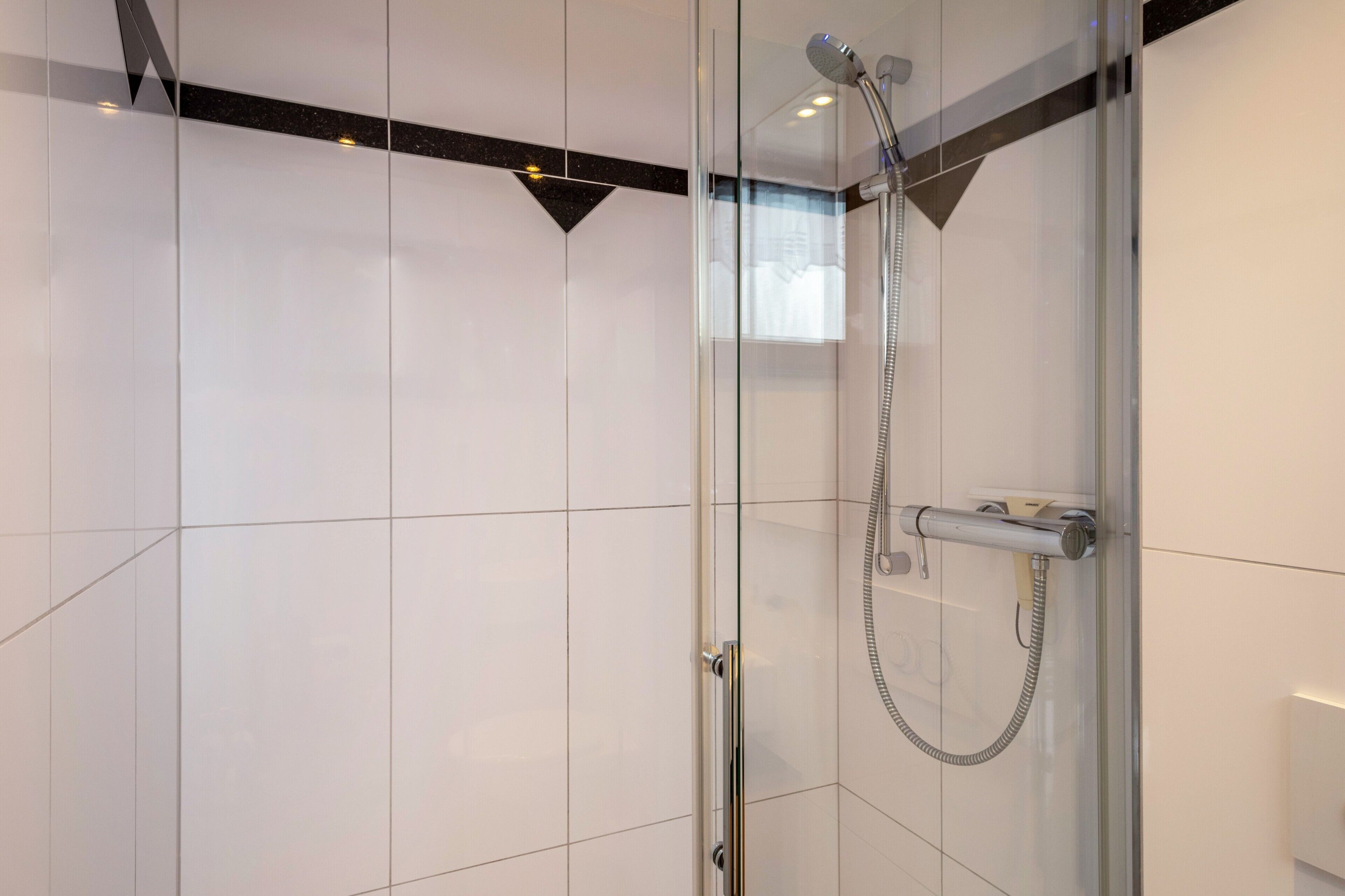 A modern shower with a glass door, a handheld showerhead, and a control panel.