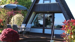 Et moderne hus med skråt tag, store vinduer og en terrasse med udendørs møbler.
