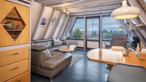 Et moderne loftrum med en alkove-seng, en sofa, et spisebord og et stort vindue med udsigt over byen.
