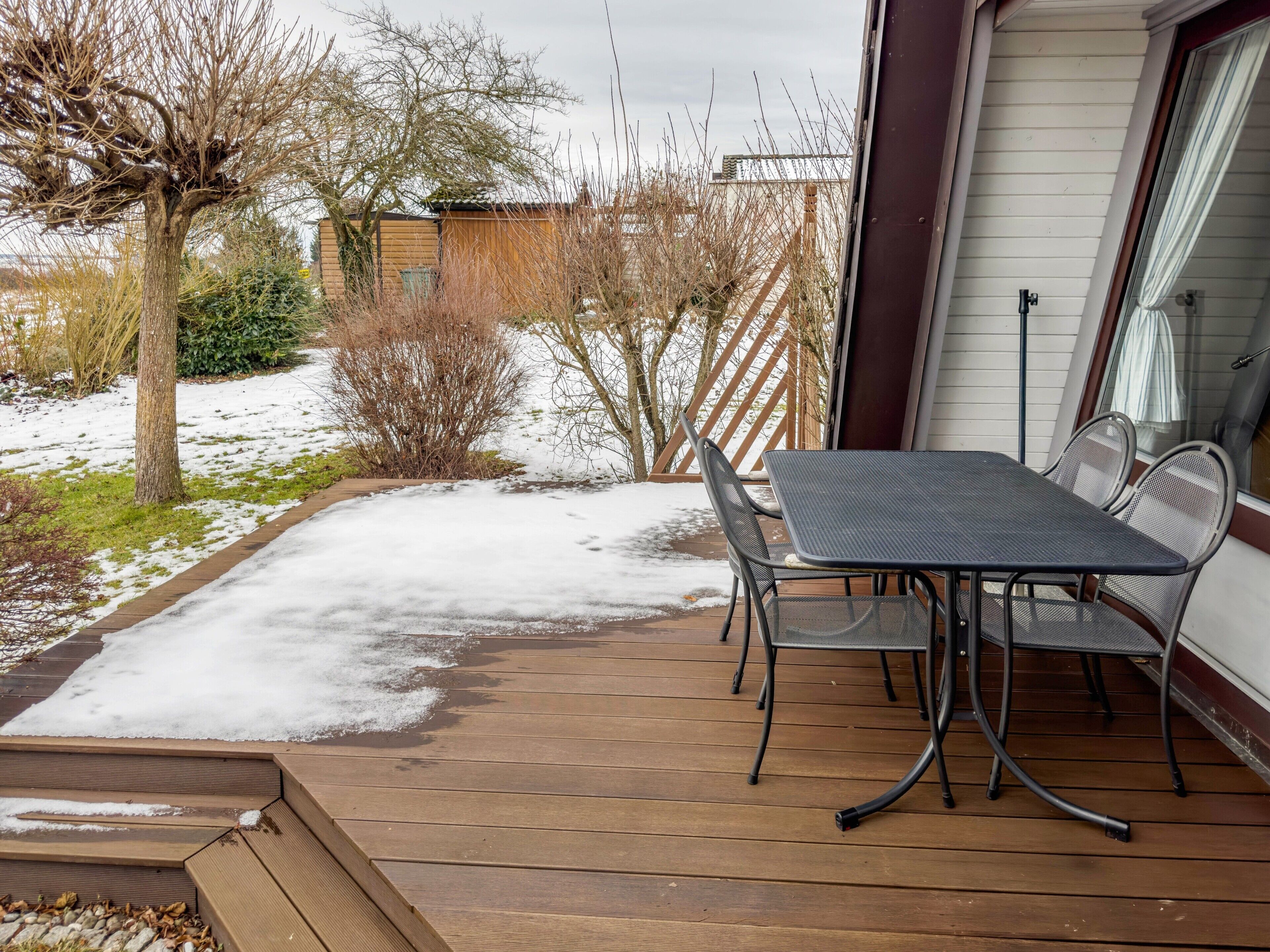 A wooden deck with a table and chairs, surrounded by snow and bare trees.