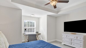 Ein Schlafzimmer mit Bett, Schreibtisch, Stuhl, Kommode, Fernseher und Deckenventilator.