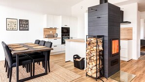 A modern kitchen with white cabinets, a black stove, and a dining area with a wooden table and chairs. - Villa Karina - Beachfront with Jacuzzi (Porvoo)