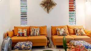 Un salon avec deux canapés orange, un pouf à motifs et un élément décoratif mural.
