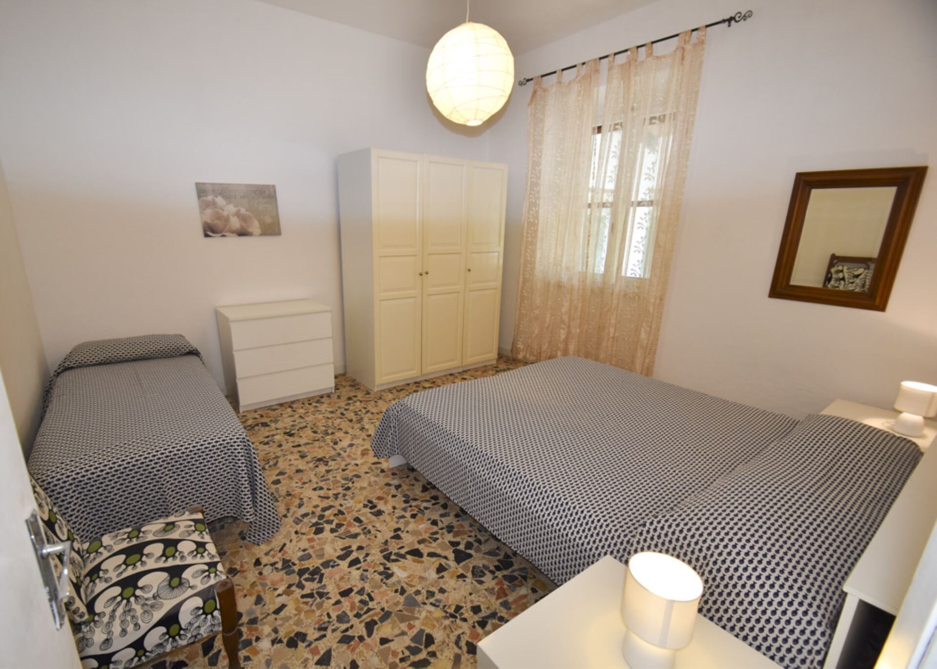 A bedroom with two beds, a wardrobe, a desk, a chair, a lamp, and a mirror.