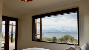 A bedroom with a large window offering a view of a body of water and trees.
