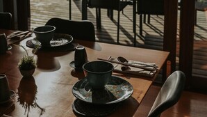A dining area with a view of the sea, featuring a table set with plates, cups, and cutlery.
