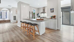 A modern kitchen with a central island, bar stools, a stainless steel refrigerator, and a microwave. - The Port Terrace (Echuca)