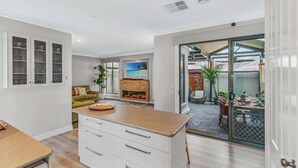 A modern kitchen with white cabinetry, a wooden countertop, and a dining area with a glass door leading outside. - The Port Terrace (Echuca)
